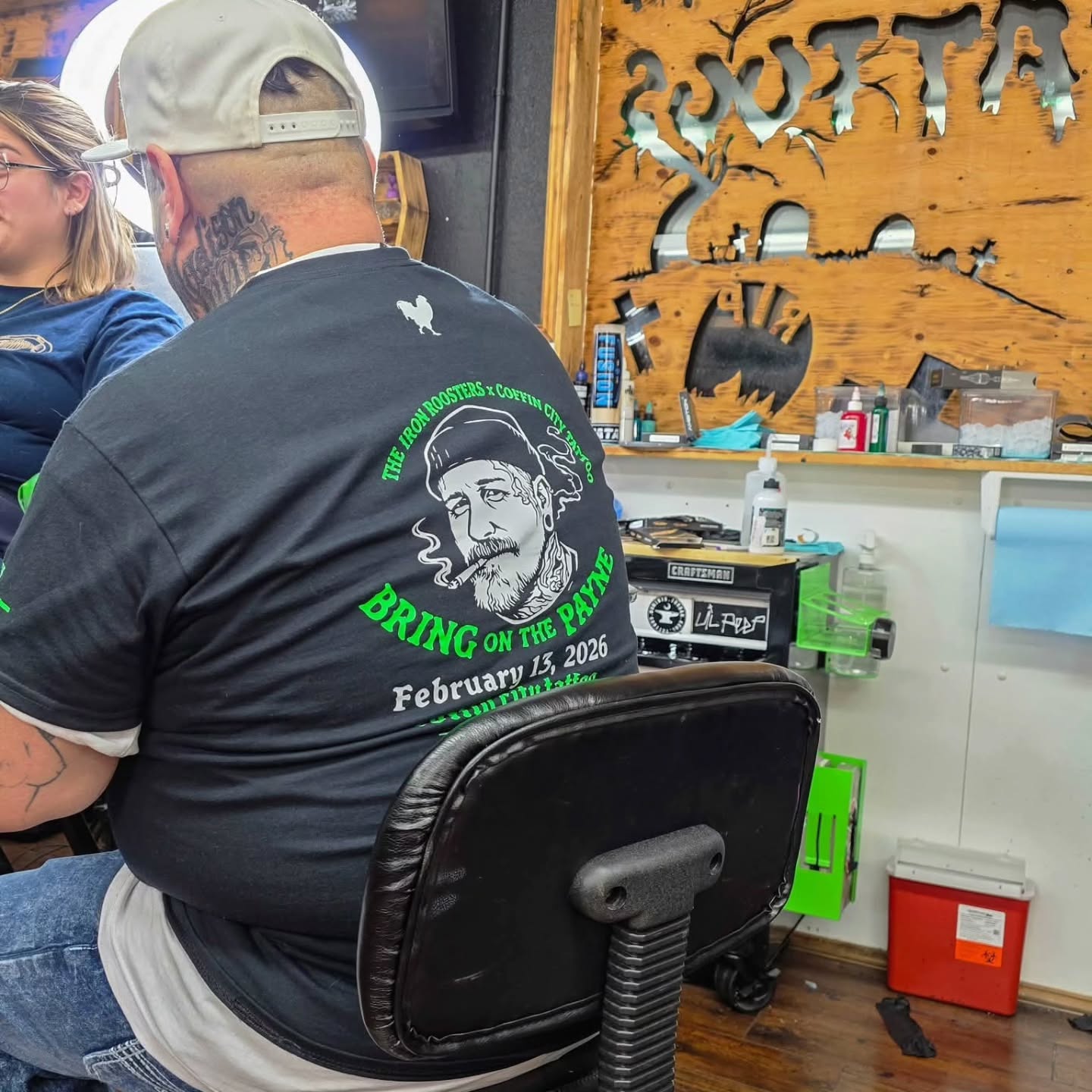 Inside Coffin City Tattoo, an artist at the station with the shop's custom Coffin City sign behind